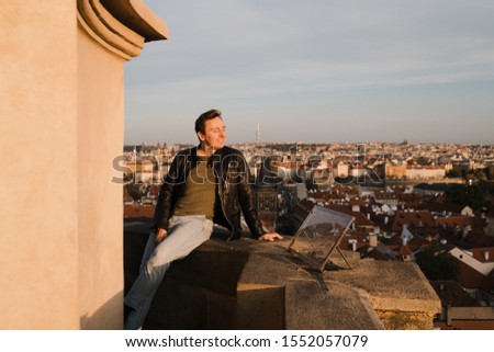 Happy man start fresh new life looking at Prague centre and Charles Bridge view from above and using phone to take a selfie photo