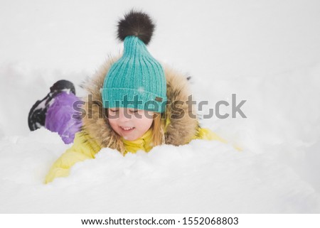 Cute happy small baby girl laying on ground in fresh fluffy white snow. Horizontal color photography.