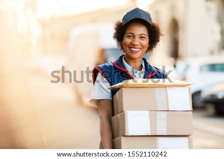 Portrait of happy black courier delivering packages and looking at the camera.  Royalty-Free Stock Photo #1552110242