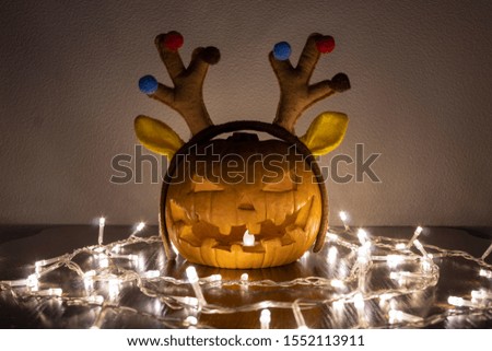 Jack O'Lantern carved pumpkin head with Christmas deer horns and garland decoration lights on Halloween