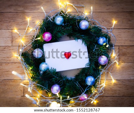 Christmas ornament and background. Very bright and tinsel,Letter with a red heart on in the middle. Green spruce and wooden floor background. Flat lay.