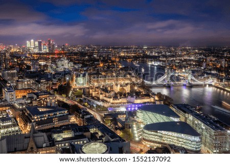 Aerial view to the illuminated skyline of London, UK, during night time featuring the famous Tower Bridge and the modern office buildings around