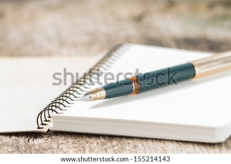 Closeup photo of notebook with old golden ink pen at wood background