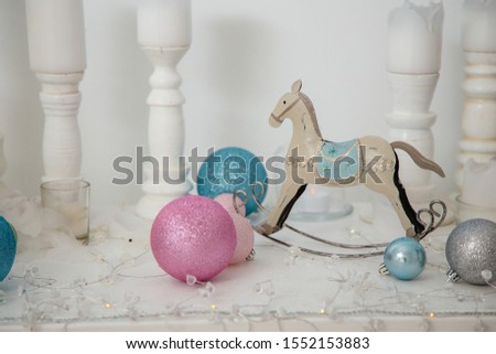 Christmas decorations, silver, blue and pink bulbs, white candles, wooden house and rocking horse toy standing on the white surface.
Merry Christmas, Happy New Year and Winter holidays concept. 