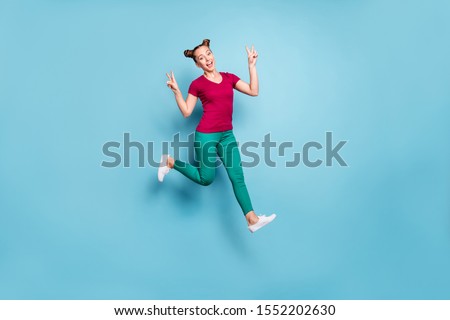 Full length body size turned photo of cheerful positive cute pretty nice charming girlfriend showing double v-sign while running and jumping isolated in pants trousers pastel color blue background
