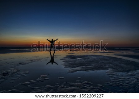 A male standing on the beach during sunset with his hands open as a sign of happiness