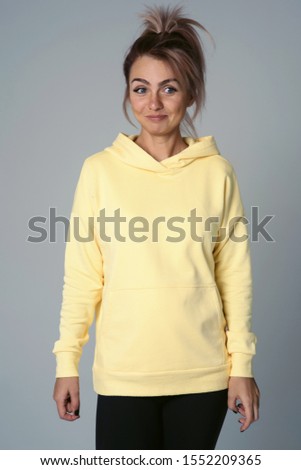 Close up of young attractive caucasian woman in yellow hoodies looking at camera posing funny, shocked with expression. Positive emotions of girl. Model tests on white background