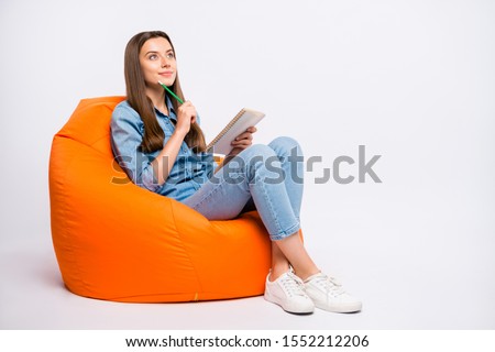 Full size profile side photo of focused girl sit on lounge chair think want create fiction story feel curious try guess ponder wear denim clothes sneakers isolated over white color background