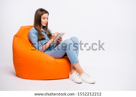 Full size profile side photo of concentrated girl write in copybook her homework for tomorrow lesson in university sit big bag armchair wear casual style clothes isolated over white color background