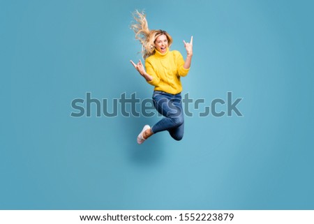 Full body photo of crazy lady jumping high enjoy metal rock concert showing hands horns excited wear knitted yellow pullover jeans isolated blue color background