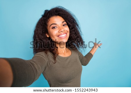 Close up photo of positive cheerful afro american tourist girl hold hand invite show her vacation take selfie video call wear casual style shirt isolated over blue color background