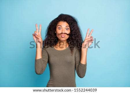 Portrait of funny funky cute childish playful girl make v-sign have fun grimace with fake mustache wear green stylish outfit isolated over blue color background