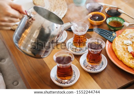 Pouring tea from tea pot to glass. Breakfast preparation concept. Traditional Turkish brewed tea drink in morning also as known "Cay" or "Turk Cayi". Relaxing or resting mood, break time concept.