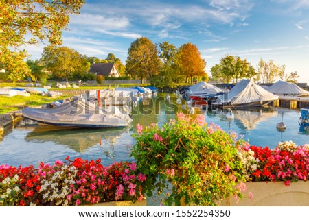 Colorful autumnal scenery of Yacht club at Geneva lake during fascinating sunrise in Switzerland. Beautiful flowers, colorful yellow trees circling the small cozy bay with sheathed recreation boats.