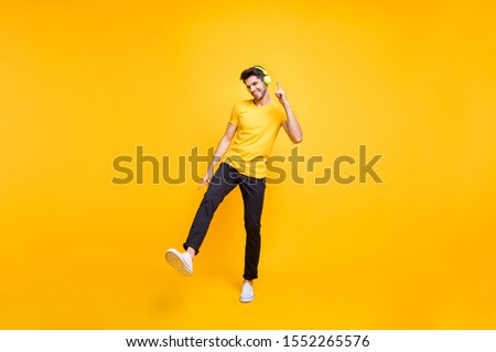 Full length photo of handsome guy at students party listening youth music earflaps dancing youngster moves wear casual t-shirt pants isolated yellow color background