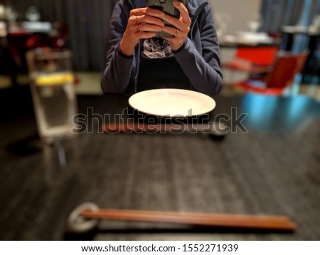 A woman sitting at a table in a restaurant using social media on her smartphone mobile app instead of talking to her companion. The background is deliberately blurred out of focus to draw attention
