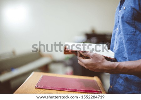 A closeup shot of a male reding the bible in the church near a wooden stand with a blurred background