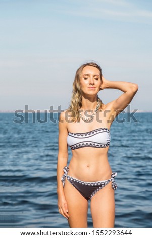 Beautiful caucasian blonde girl with make-up in a bathing suit on a background of the sea enjoys relaxation and the sun. Summer holidays and tourism concept.