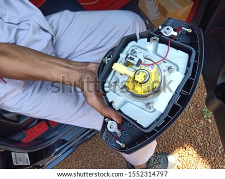 the technician in uniform holding the airbag panel that take off from the steering wheel in passenger cabin of the car between onsite service Royalty-Free Stock Photo #1552314797