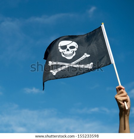 skull flag in hand waving on blue sky background.