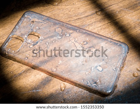 Wet smartphone softcase on wooden board. 