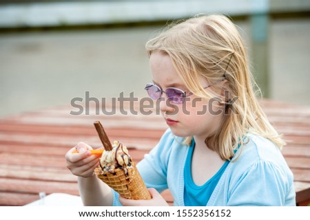 Pretty young blonde girl wearing purple sunglasses and enjoying a large ice cream with chocolate flake