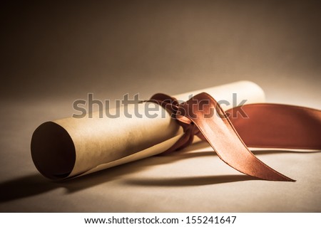 A parchment diploma scroll, rolled up with red ribbon laid at an oblique angle.  Processed to give a vintage or retro appearance. Royalty-Free Stock Photo #155241647
