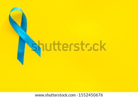 Blue ribbon as symbol disease control on yellow background top view copy space