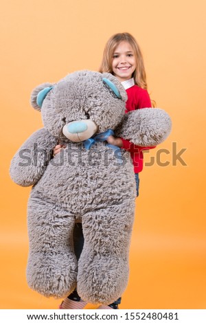 Happy childhood concept. Kid with animal doll, present and gift. Child smile with grey soft toy. Holiday, birthday, anniversary celebration. Girl hold big teddy bear on orange background.