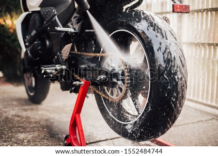 Washing motorcycle chain with high pressure jet, close-up.