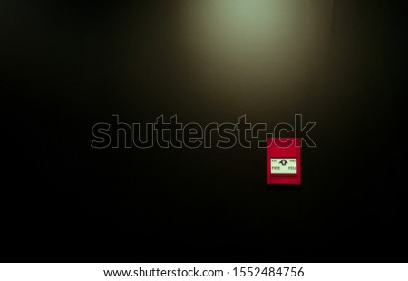 Red fire alarm pull station on black wall background. Fire alarm switch. Emergency safety system. Fire alarm on dark concrete wall. Warning and security system. Red box for safety alert on wall.