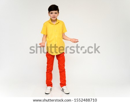 Teenager Schoolboy Boy Concept Shows Emotion. Full-length photo of a child in red pants and a yellow shirt on a white background in studio. Stands in front of the camera in various poses.