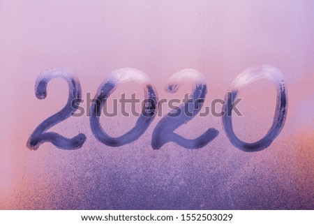 2020. Handwritten text on frosted window. Purple background, misted up glass. Foggy rainy window. New Year banner, blue card. Concept of calendar date. 