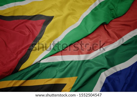waving colorful flag of south africa and national flag of guyana. macro