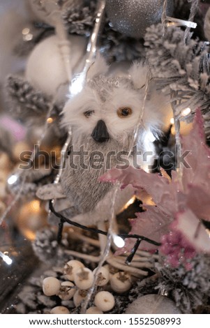 Christmas toy owl close-up on a decorated Christmas tree. Blurred background and lights from a garland. Delicate colors in pink with gray.