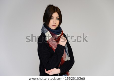 Close-up portrait of a young pretty girl student with long black hair with a scarf and in a sweater, on a white background. Standing right in front of the camera in different poses with emotions.