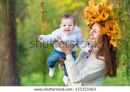 Attractive young mother holding a baby girl in an autumn forest with a maple leaf wreath on her head
