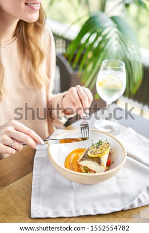Roasted Halibut with vegetables, paprika pepper and pumpkin cream. Lunch in a restaurant, a woman eats delicious and healthy food. Dish decorated with a slice of lemon. Restaurant menu