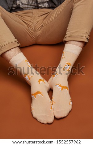 Close-up shot of male legs in turned-up brown jeans and beige socks with shiba inus print. The photo is made on the brown background.