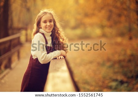 adorable preteen child looking at the camera standing on wooden bridge in the park at fall time
