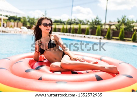 Young girl having fun and laughing on an inflatable giant watermelon pool float mattress in a bikini.