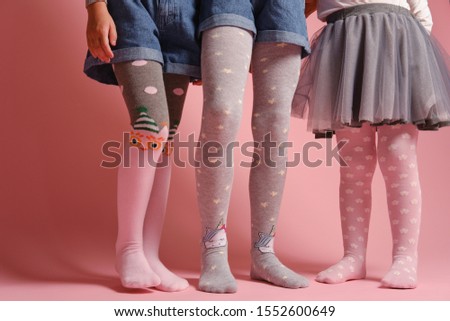 Girlish legs in pantyhose on a pink background. A collection of childrens tights for girls. A variety of knitted tights. Childrens clothes. Childrens fashion. Legs and feet of a group of girls