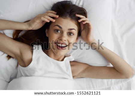 A woman in a sundress lies on a soft bed with a blanket pillow