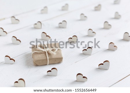 Handmade gift in kraft paper on a white background. Wooden decorative hearts around gift. Valentine or other holiday.