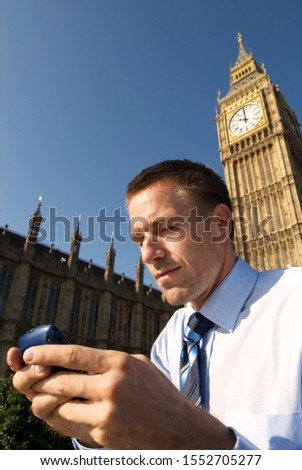 Young businessman in shirt and tie stands texting in front of the London skyline with Big Ben and the Houses of Parliament on a bright sunny day