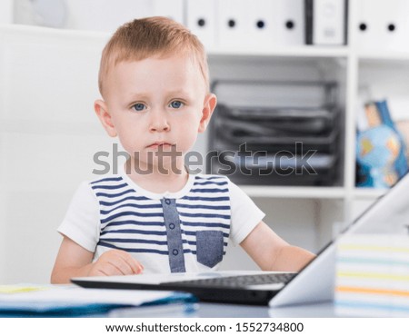 Cute kid is playing on laptop in the office.