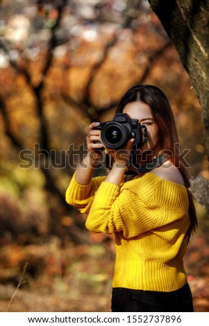 woman photographer takes pictures and covering her face with the camera. the photographer in action in autumn