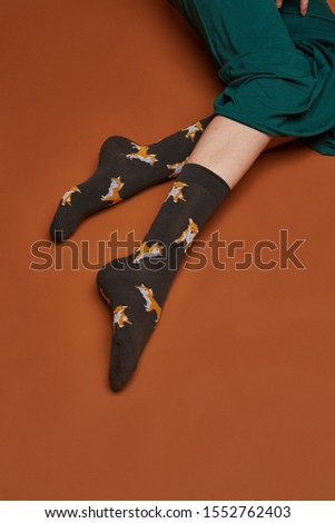 Close-up shot of female legs in wide green trousers and black socks with shiba inus print. The photo is made on the brown background.