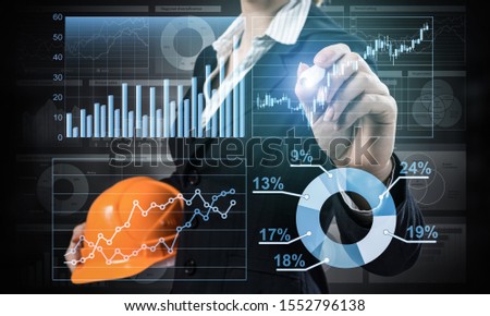 Businesswoman pointing on 3d financial chart. Woman in business suit standing with safety helmet. Digital technology and innovation in construction industry. Economy and investment data visualization.