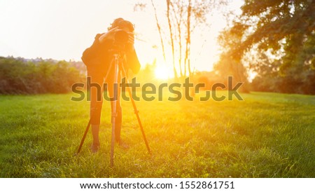 Nature photographer with camera on tripod while photographing in a countryside at sunset